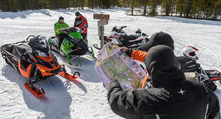Snowmobilers looking at a map on a trail